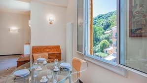 Un coin repas avec une table en verre dressée pour quatre personnes, une commode en bois et une grande fenêtre donnant sur une colline verdoyante.