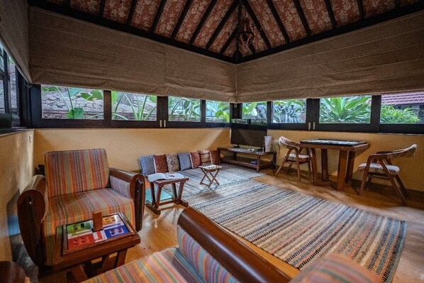 A spacious room with a high ceiling, large windows, a sofa, a small table, and a chair. - Brij Paraiso Saligao, Goa | An Indo-Portuguese Villa (Saligao)