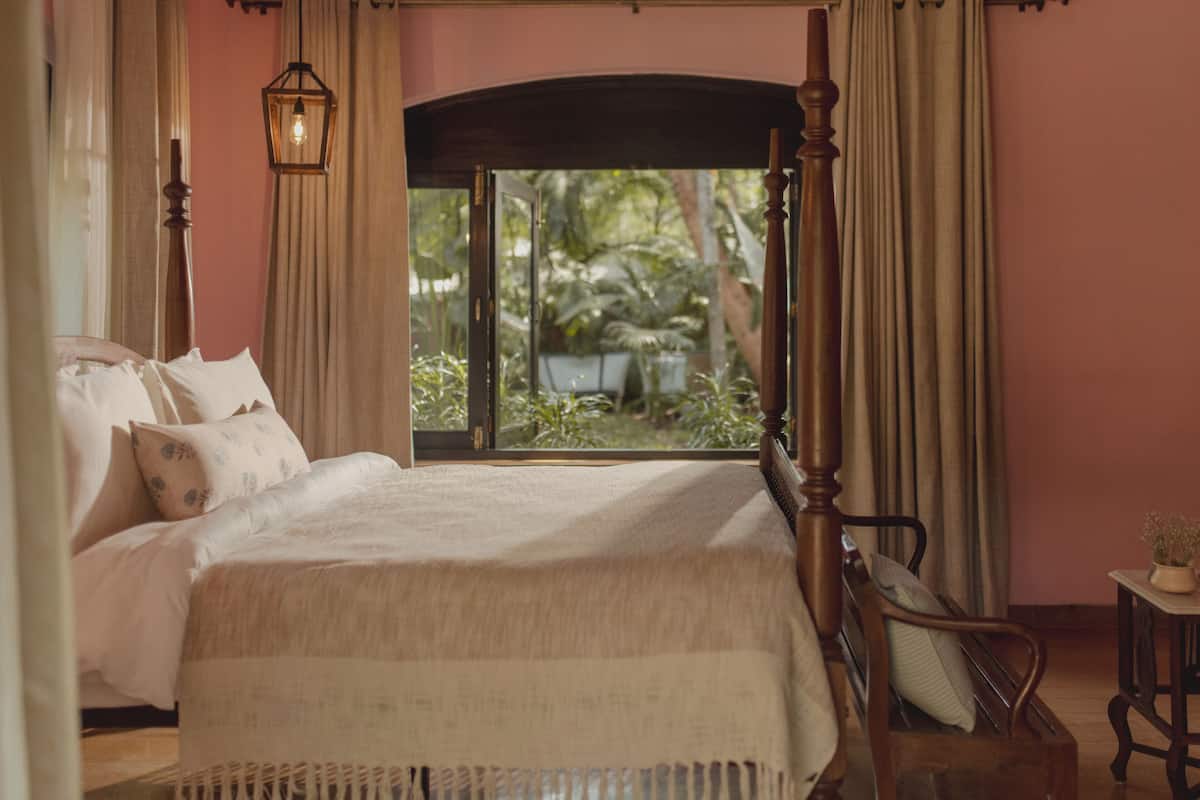 A bedroom with a large bed, a nightstand, a chair, and a window with curtains.