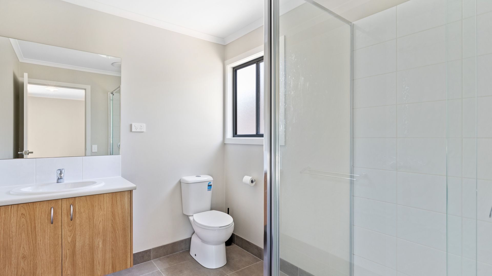 Une salle de bain avec un lavabo blanc, des meubles en bois, des toilettes et une cabine de douche en verre.