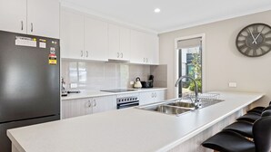 Een moderne keuken met witte kasten, een roestvrijstalen koelkast, een inbouwoven en een groot raam dat voor natuurlijk licht zorgt.
