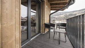 A wooden balcony with two black chairs and a table, overlooking a mountainous landscape. - Apartment in Kirchberg Near Schaterzlift (Kirchberg in Tirol)
