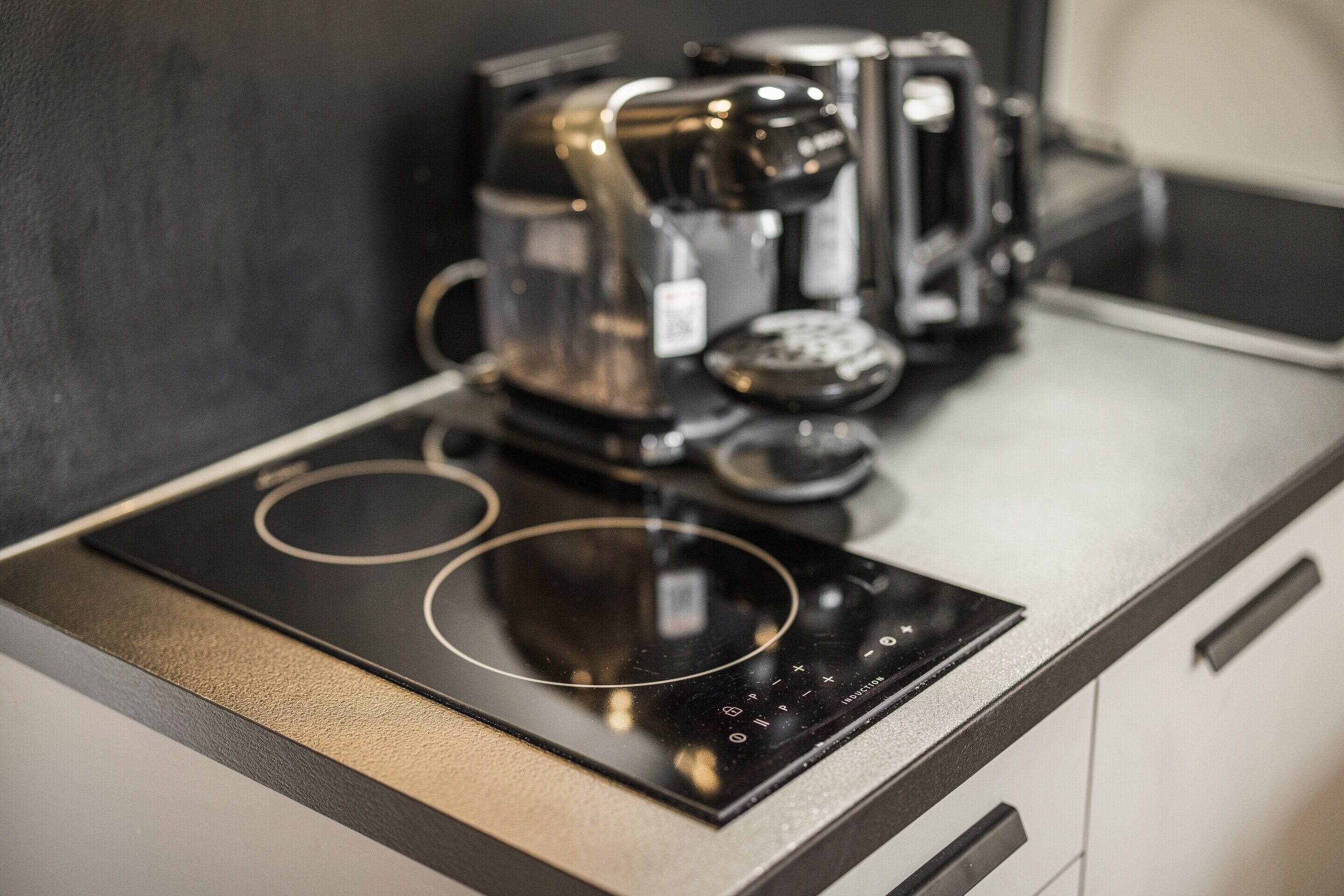 Eine Küche mit einer schwarzen Induktionskochplatte und einer Kaffeemaschine.