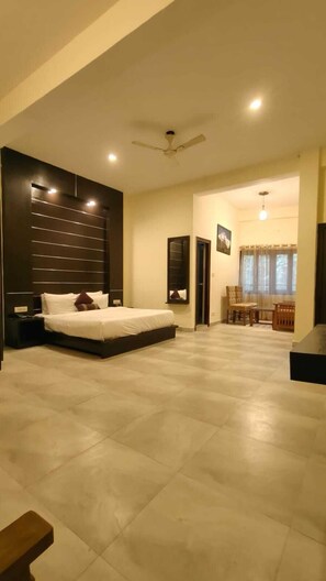A spacious bedroom with a large bed, a ceiling fan, and a dining area with a table and chairs. - Holiday Highlight By Golden Castle Hotel (Ramnagar)