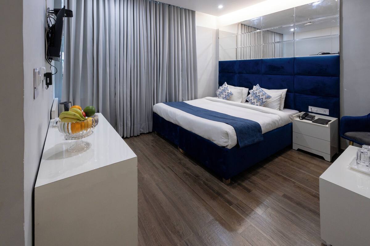 A modern hotel room with a large bed, a bedside table, a desk, and a fruit bowl.