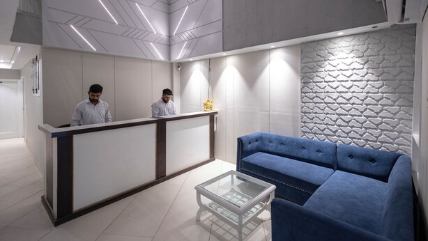 A reception area with a modern design, featuring a reception desk, two staff members, a blue sofa, and a glass coffee table. - Hotel Downtown (Chandigarh)