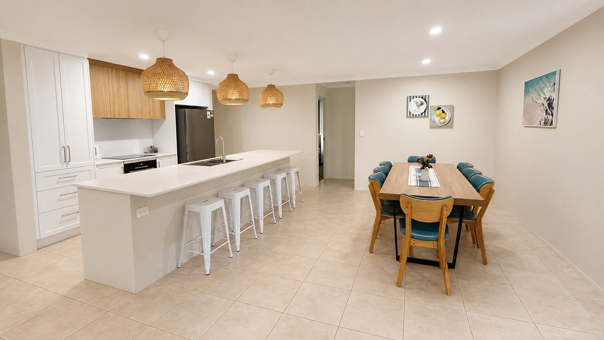 A modern kitchen with a central island, white bar stools, and a dining table with chairs.