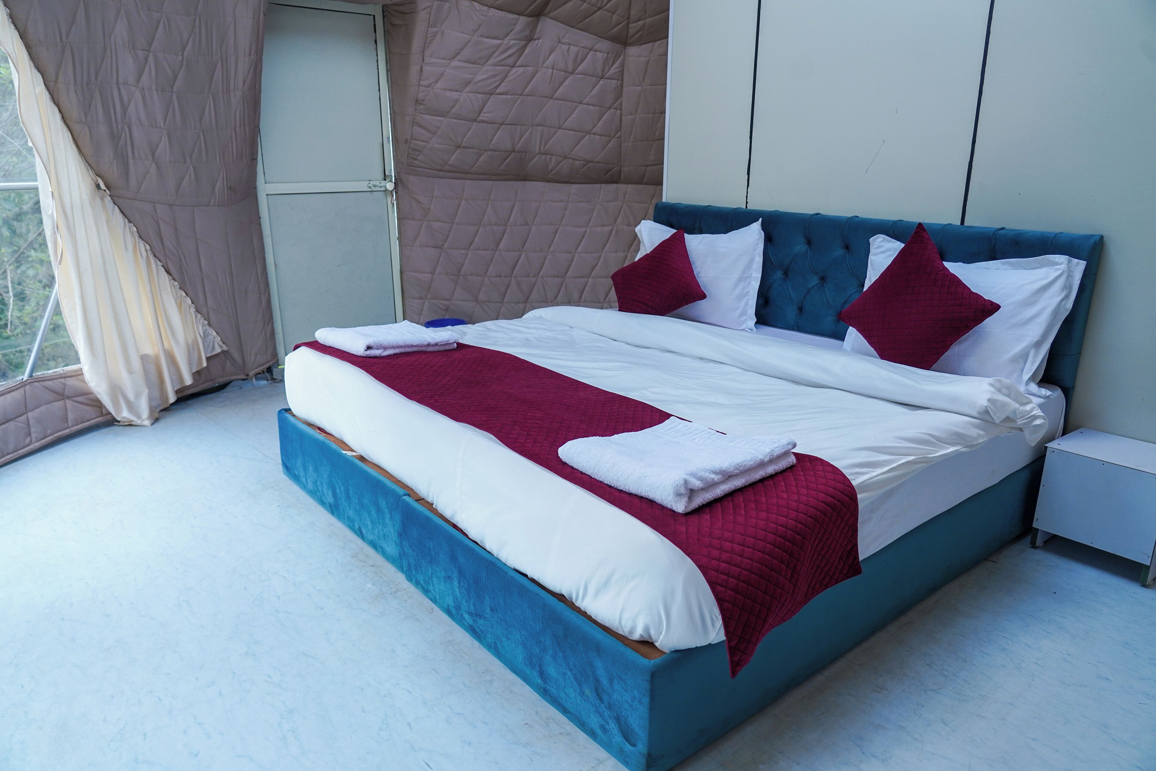 A neatly made bed with a blue headboard, white and red bedding, and a red throw blanket.
