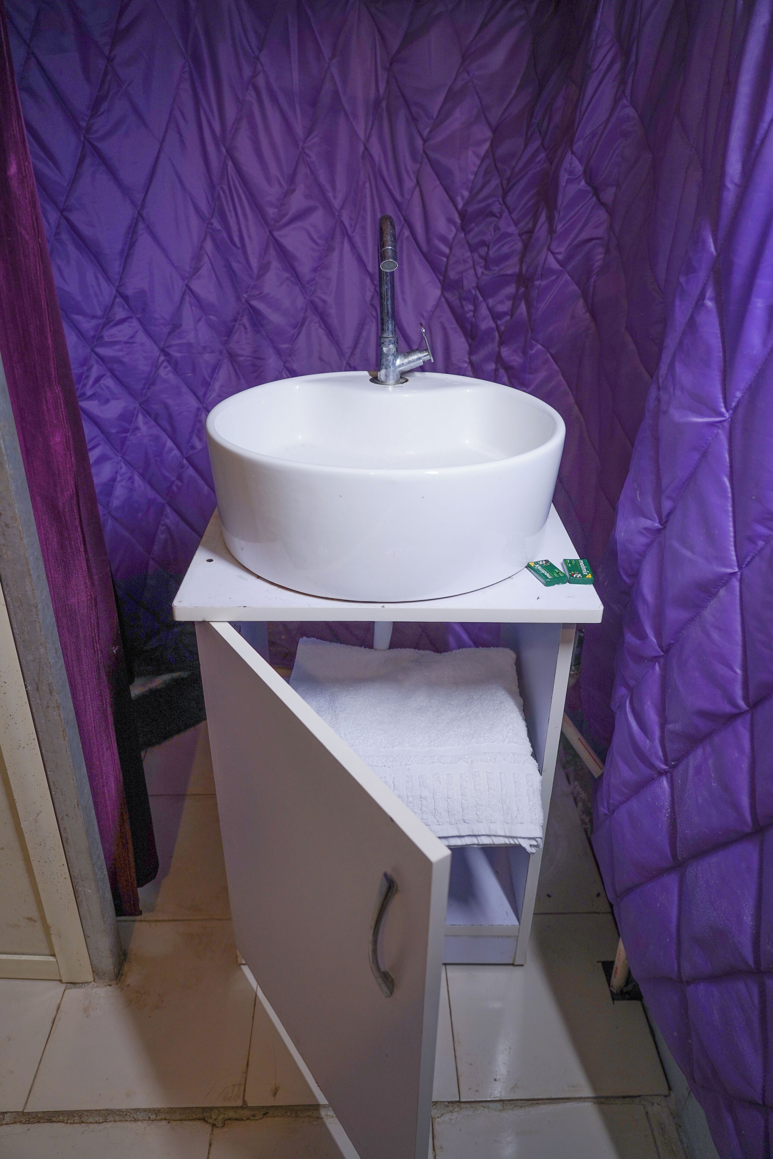 A bathroom with a white sink, purple walls, and a white towel on a shelf.
