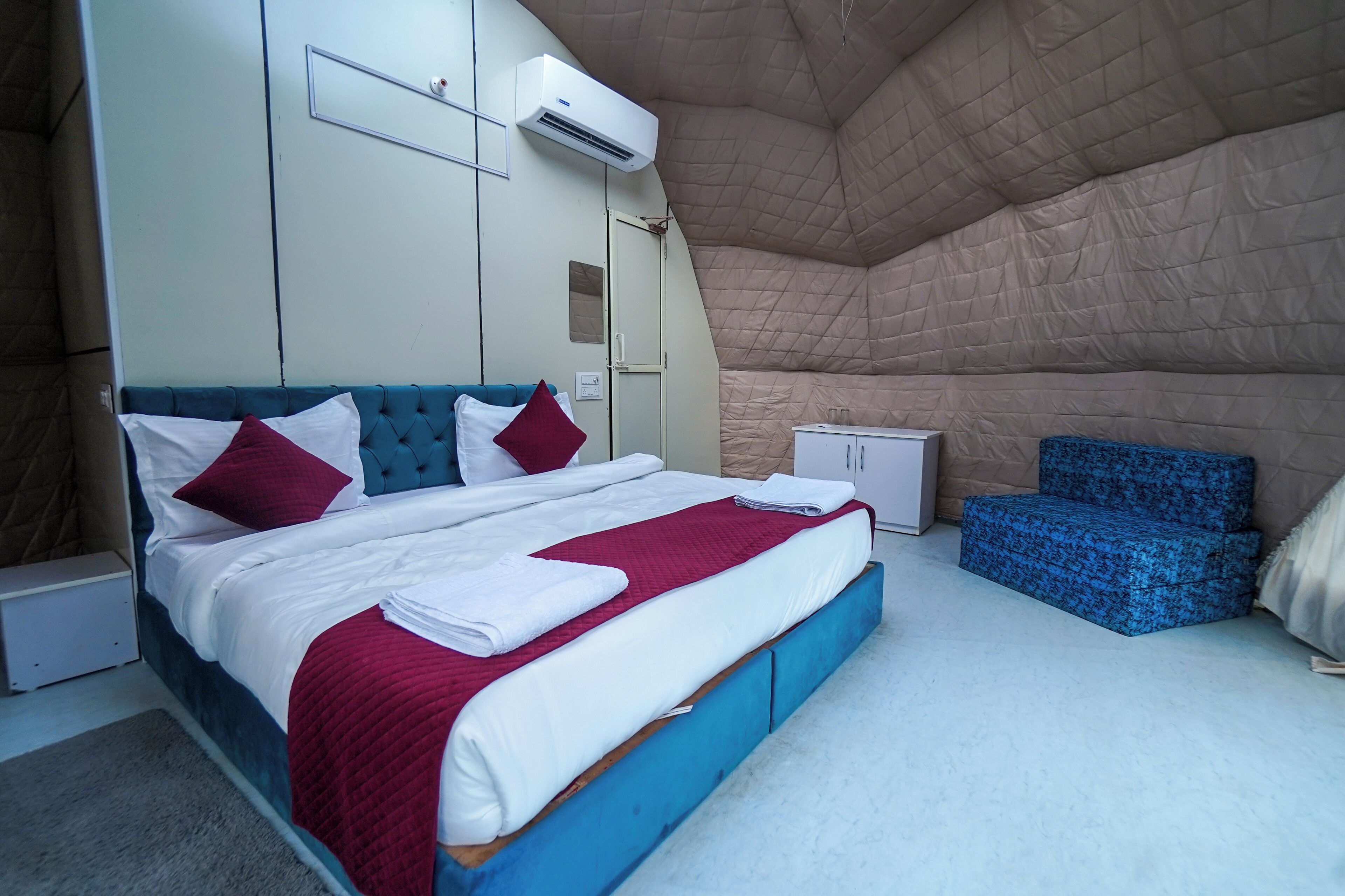 A bedroom with a large bed, a wardrobe, a small cabinet, and a blue chair.