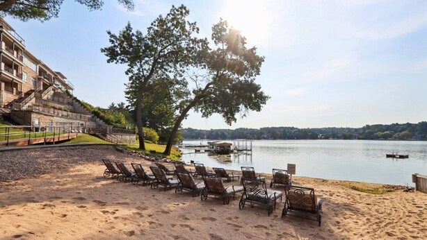 A beach with sun loungers and a view of a lake. - Vacation Awaits at Delton Grand (Wisconsin Dells)