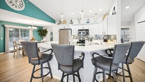 A modern kitchen with a central island, bar stools, and a clock on the wall. - Vacation Awaits at Delton Grand (Wisconsin Dells)