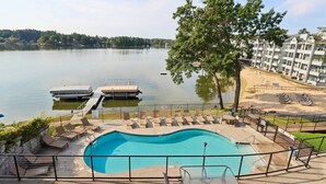 A swimming pool with lounge chairs, a dock, and a view of a lake and buildings in the background. - Vacation Awaits at Delton Grand (Wisconsin Dells)