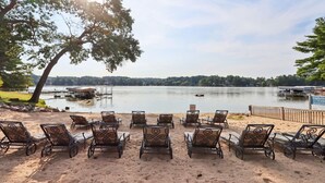 A lakeside seating area with metal chairs and tables, a sandy beach, and a dock with boats. - Vacation Awaits at Delton Grand (Wisconsin Dells)