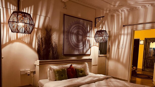 Une chambre à coucher avec un grand lit, deux luminaires suspendus, une tapisserie murale et une porte dotée d’un miroir.