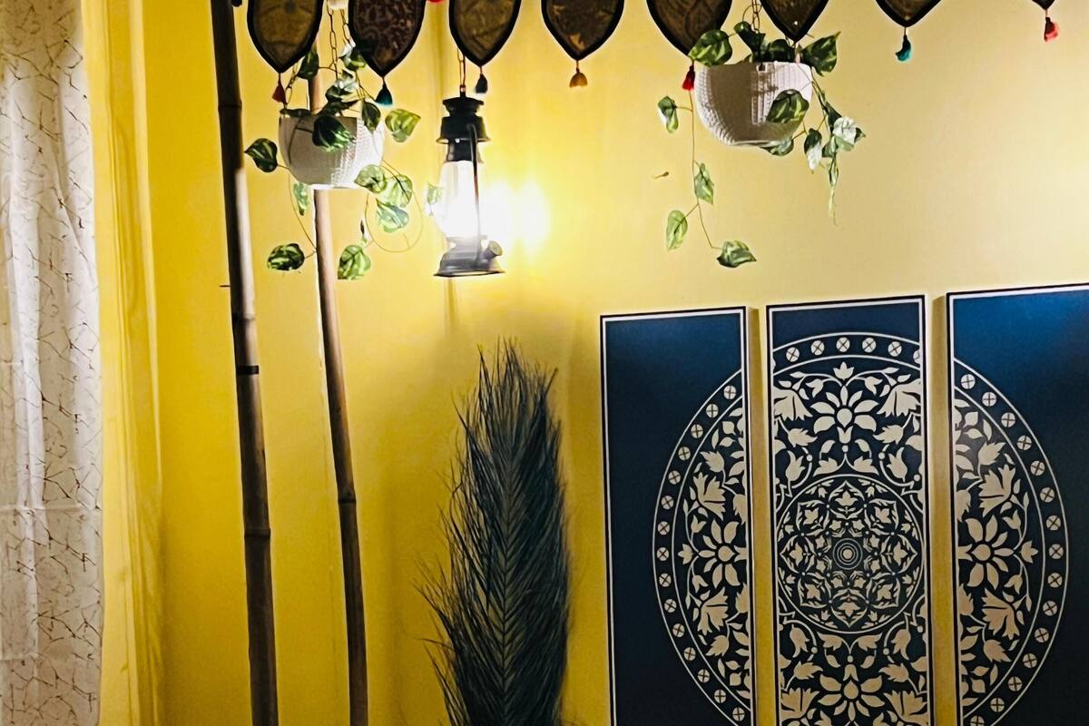 Una habitación con una pared amarilla, una cama con ropa de cama estampada y decoración en la pared.