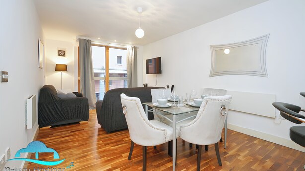 Un coin repas avec une table en verre, des chaises blanches et un canapé en arrière-plan.