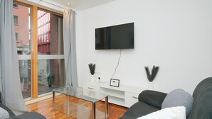 Un salon moderne avec une table basse en verre, un canapé gris et un téléviseur à écran plat fixé au mur.