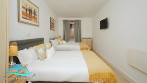 Une chambre d’hôtel avec deux lits, une télévision, une fenêtre avec des rideaux et des œuvres d’art accrochées aux murs.