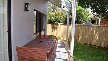 A patio with a table and chairs, a wooden fence, and a building in the background.