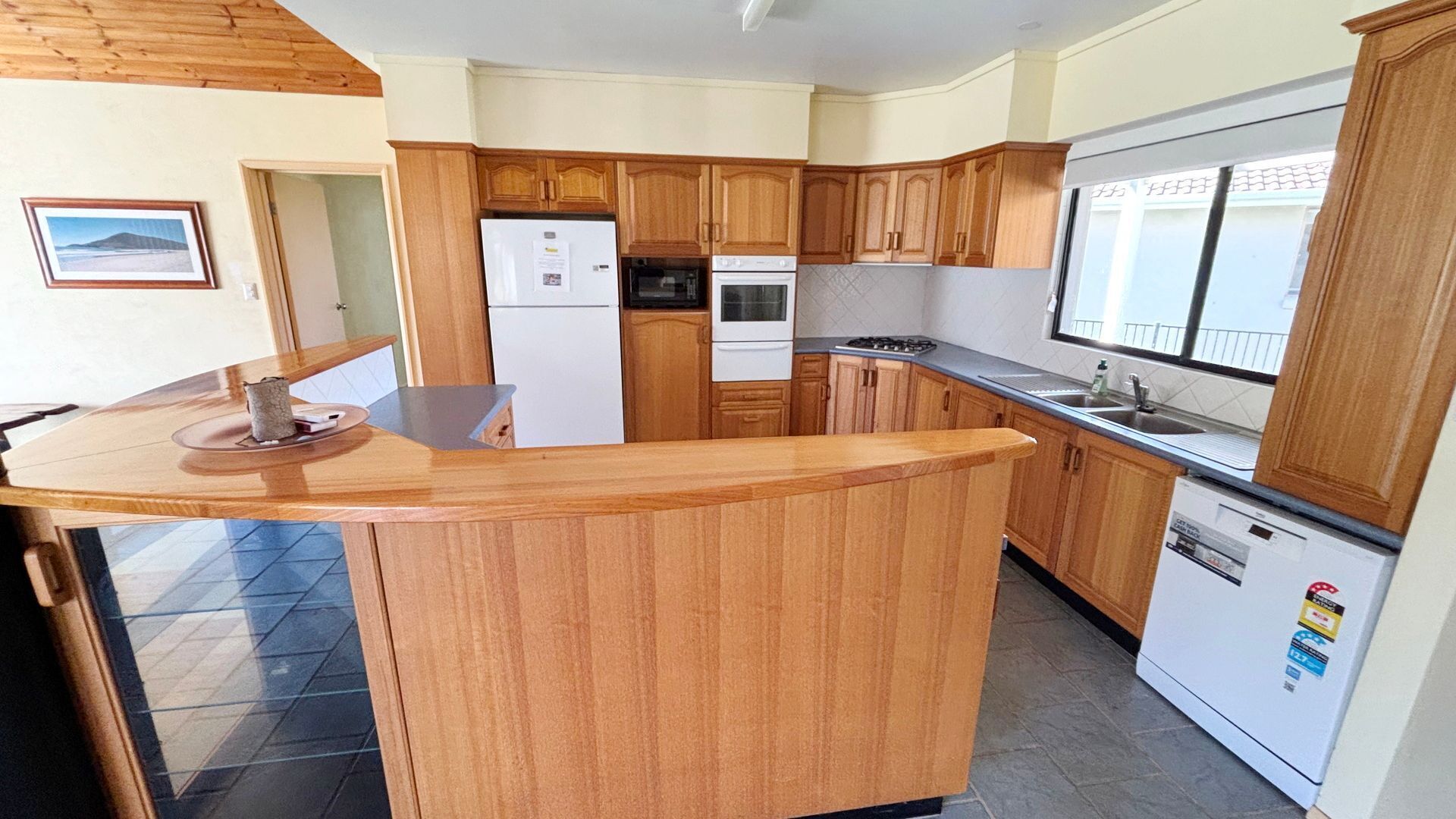 A kitchen with wooden cabinets, a refrigerator, an oven, a sink, and a window.