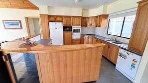Eine Küche mit Holzausstattung, einem Kühlschrank, einem Backofen, einer Spüle und einem Fenster.