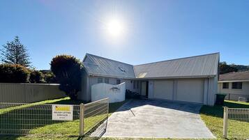 A two-story building with a metal roof, a driveway, and a fenced area with a sign for holiday letting.