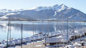 Una marina con barche coperte di neve, cielo sereno e montagne innevate sullo sfondo.