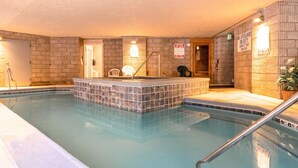 Una piscina interna con area solarium piastrellata, segnali di sicurezza e una sedia per il bagnino.