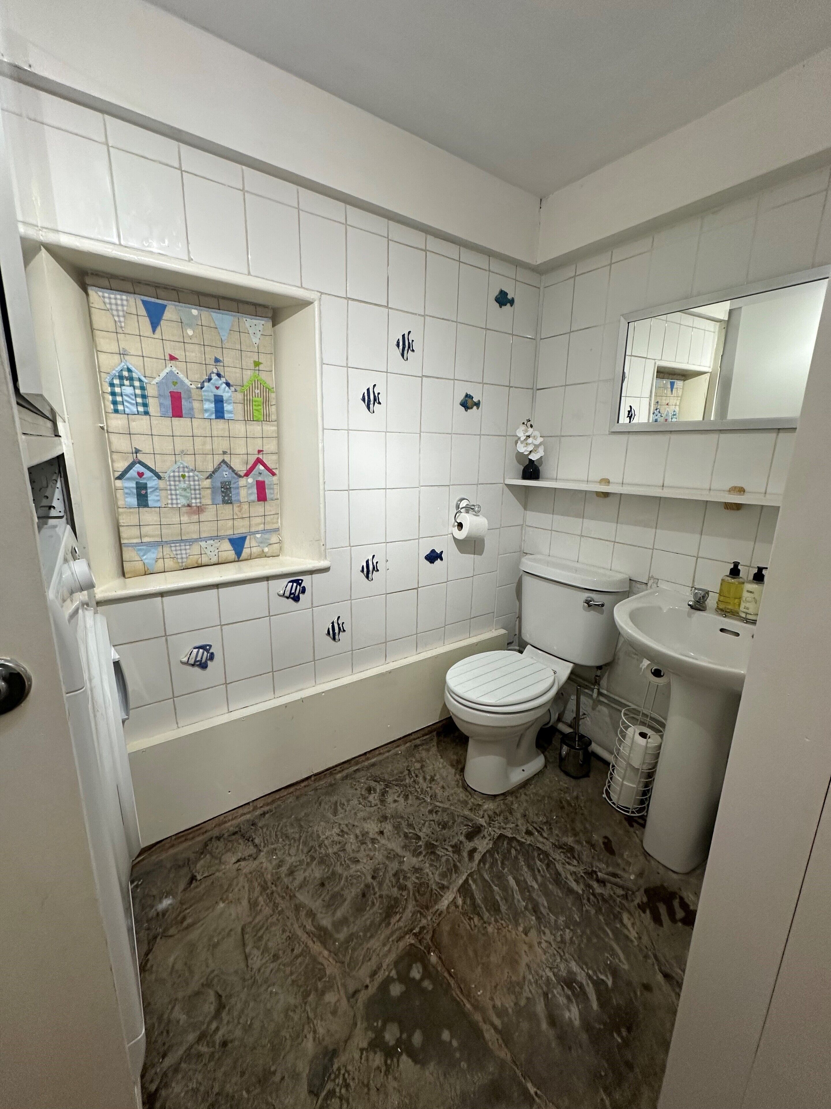 Un baño con inodoro, lavamanos y ventana con vista decorativa a casas.