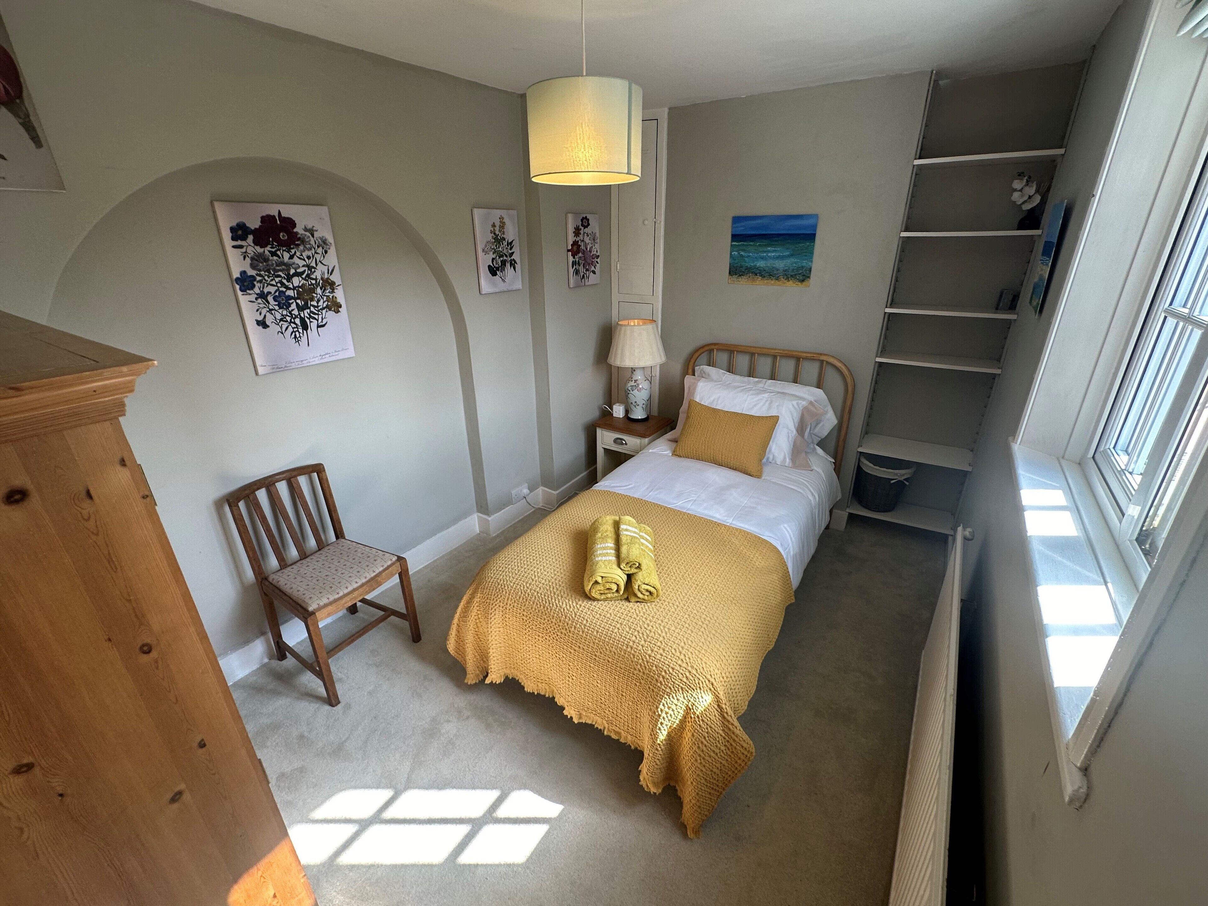 A bedroom with a bed, a chair, a nightstand, a lamp, and a window.