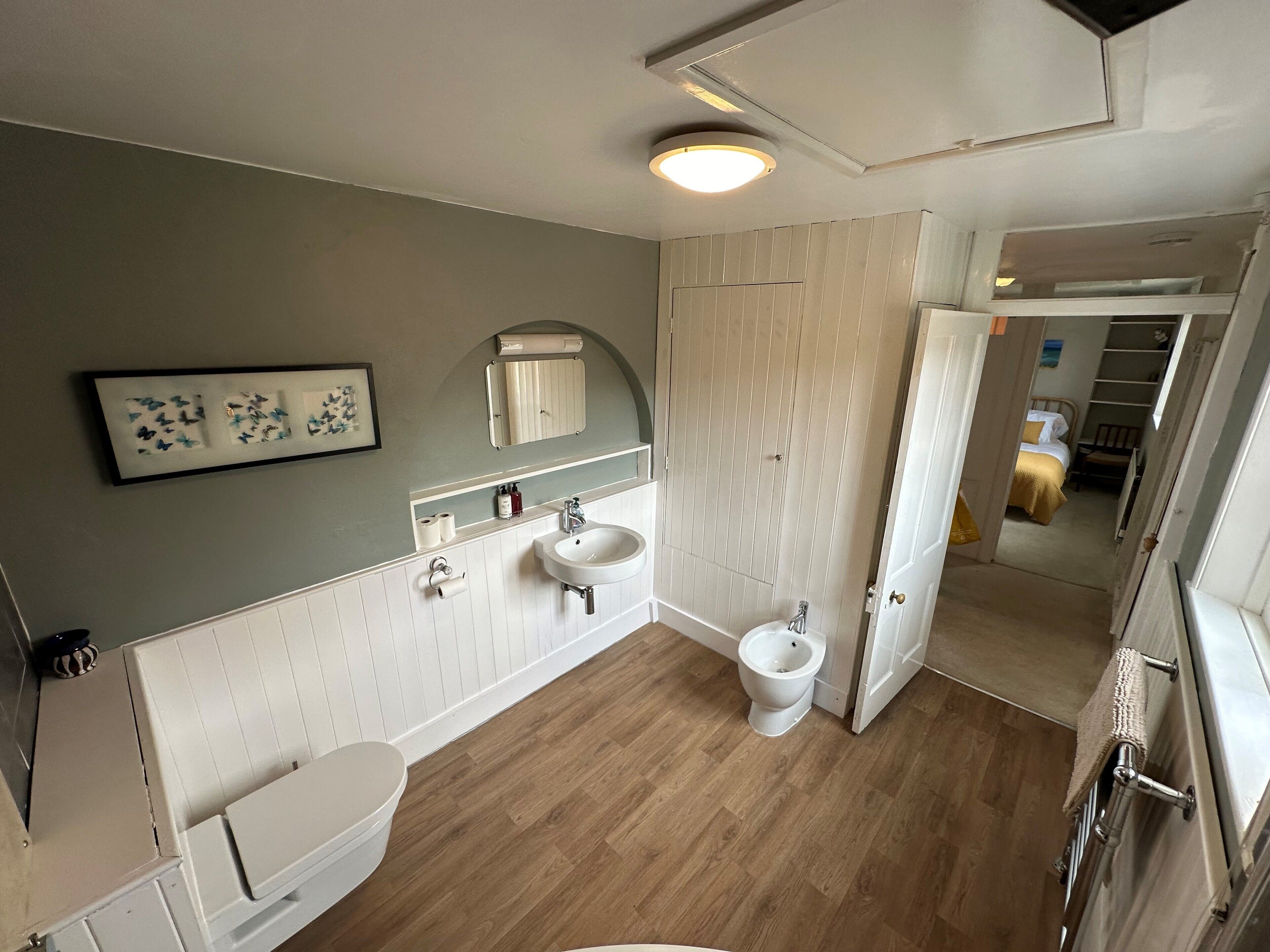 A bathroom with a toilet, sink, and bidet. There is a mirror above the sink and a framed picture on the wall.