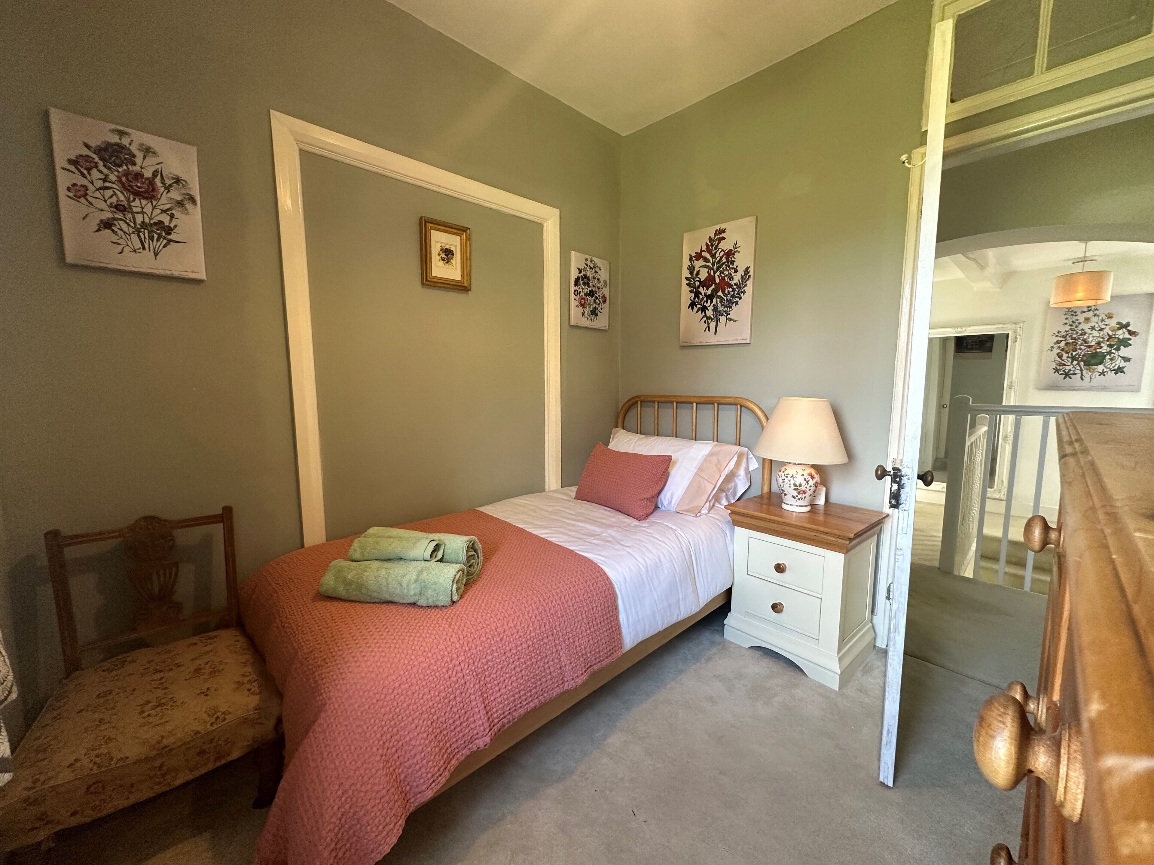 Un dormitorio con cama, mesita de noche, silla y puerta que da a otra habitación.
