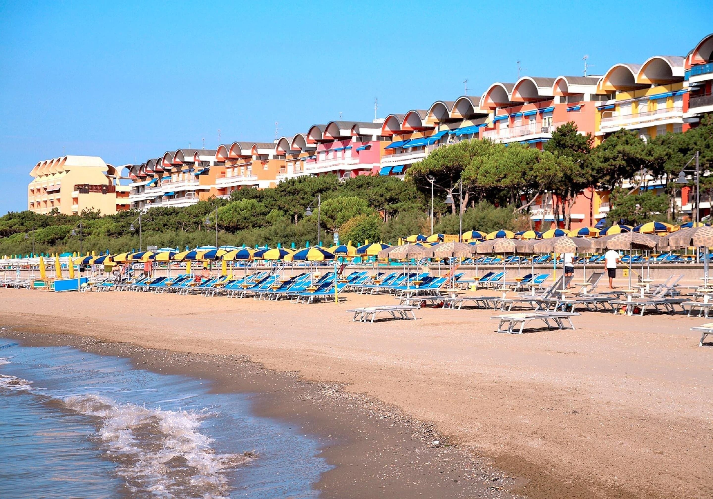 Un hotel frente a la playa con varios balcones, sillas de descanso y sombrillas.