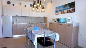 A kitchen with white cabinets, a dining table with chairs, and a painting of a beach scene on the wall. - Porto Santa Margherita Beach Stay (Caorle)