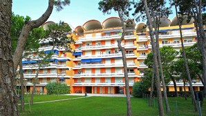 A multi-story hotel with balconies, a grassy courtyard, and trees. - Porto Santa Margherita Beach Stay (Caorle)