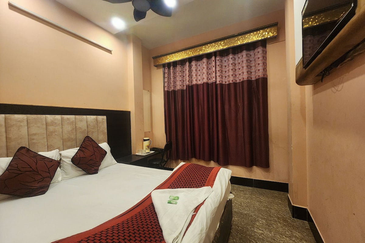 Una habitación de hotel con cama, mesita de noche, escritorio, silla, ventana con cortinas y ventilador de techo.