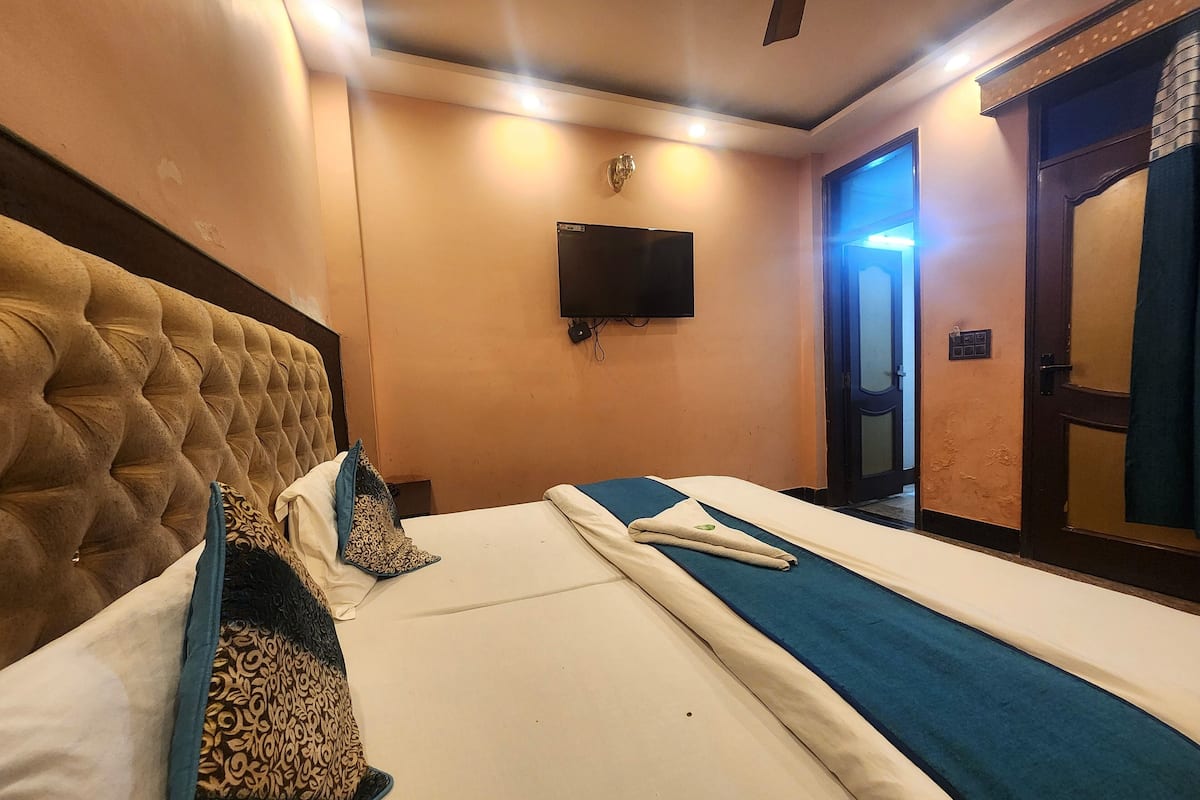 Habitación de hotel con una cama grande, un televisor de pantalla plana montado en la pared y una puerta que da a otra habitación.