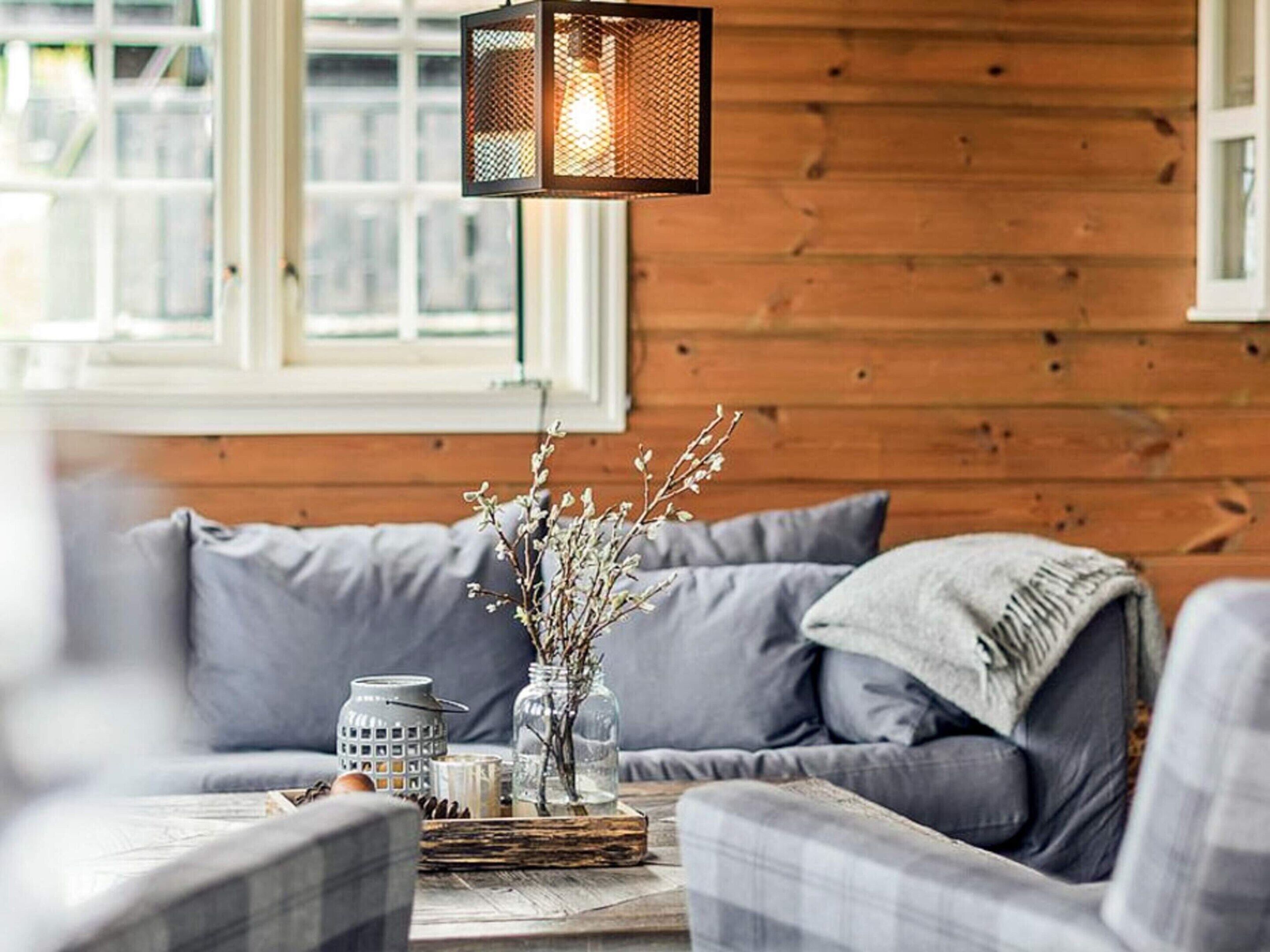 A cozy living room with a wooden wall, a gray sofa, and a hanging lantern.
