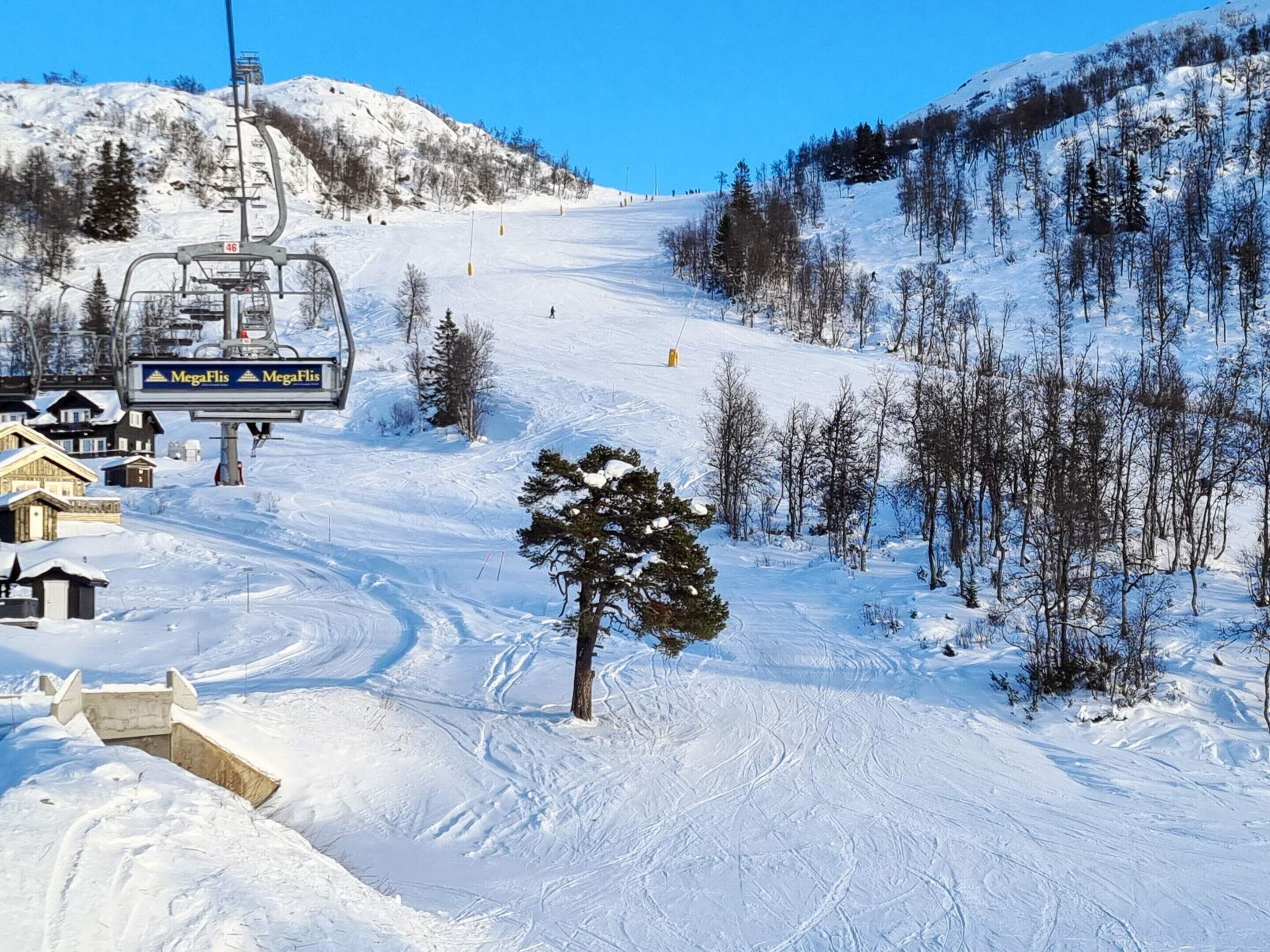 Un telesilla con señalización 'MegaFlis', una pendiente nevada y escasos árboles.