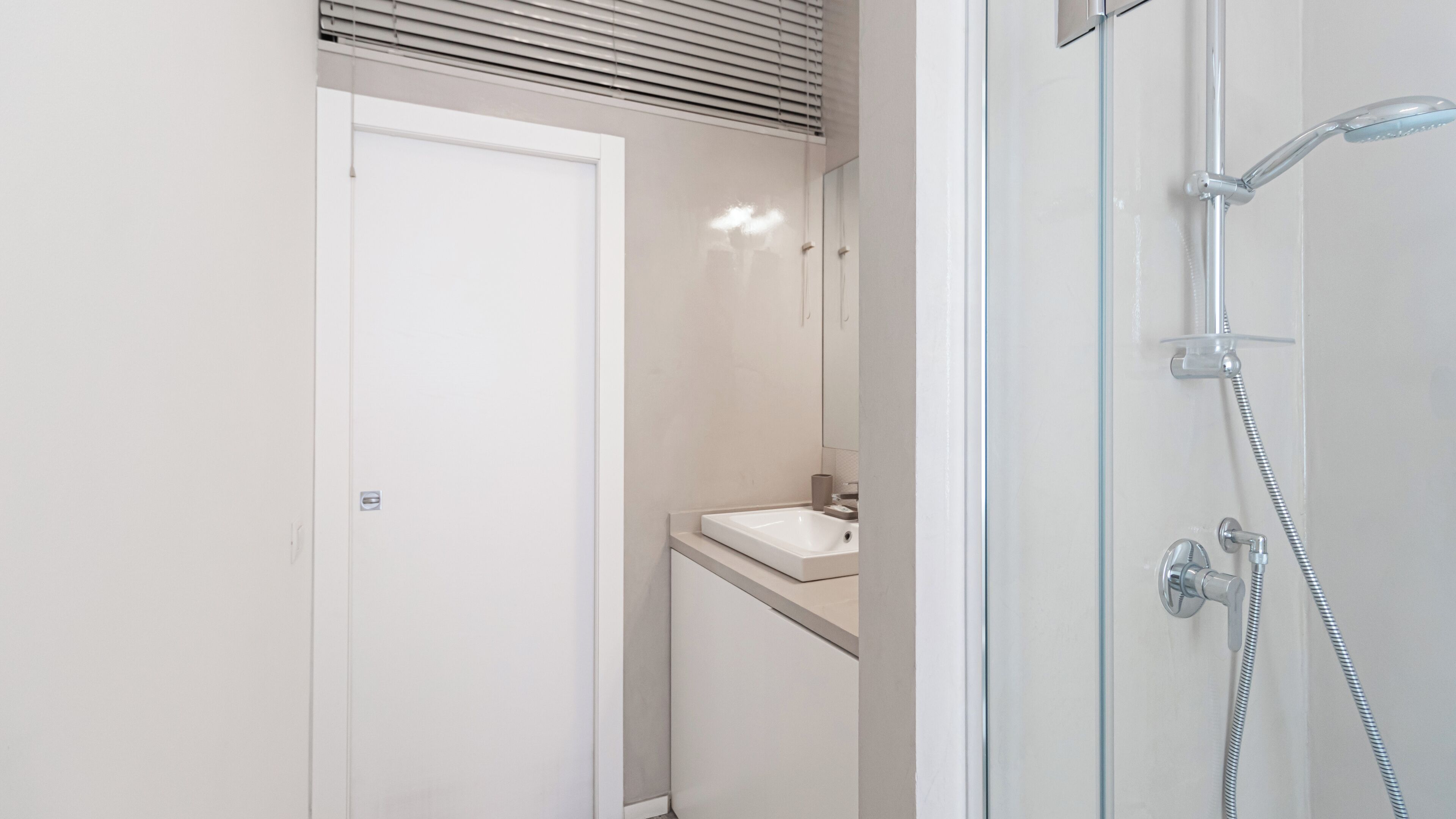 Une salle de bain moderne avec une douche à parois de verre, un lavabo blanc et une porte donnant sur une autre pièce.