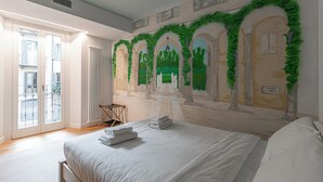 Ein Hotelzimmer mit einem großen Bett, einem Wäscheständer, Blick ins Freie und einem Wandgemälde.