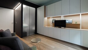 Ein modernes Wohnzimmer mit einer Couch, einem kleinen runden Tisch und einem Fernseher auf einem Holzregal.