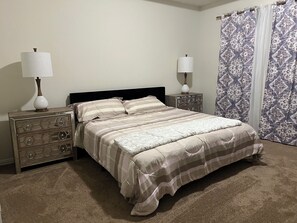 Een slaapkamer met een bed, twee nachtkastjes, een dressoir en een raam met gordijnen.