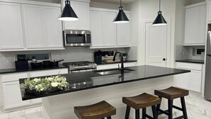 A modern kitchen with white cabinetry, a stainless steel stove, black countertops, and two bar stools. - Relax in Style at Our Missouri City Getaway (Missouri City)
