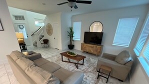 A modern living room with a beige sofa, a coffee table, and a TV cabinet. - Relax in Style at Our Missouri City Getaway (Missouri City)