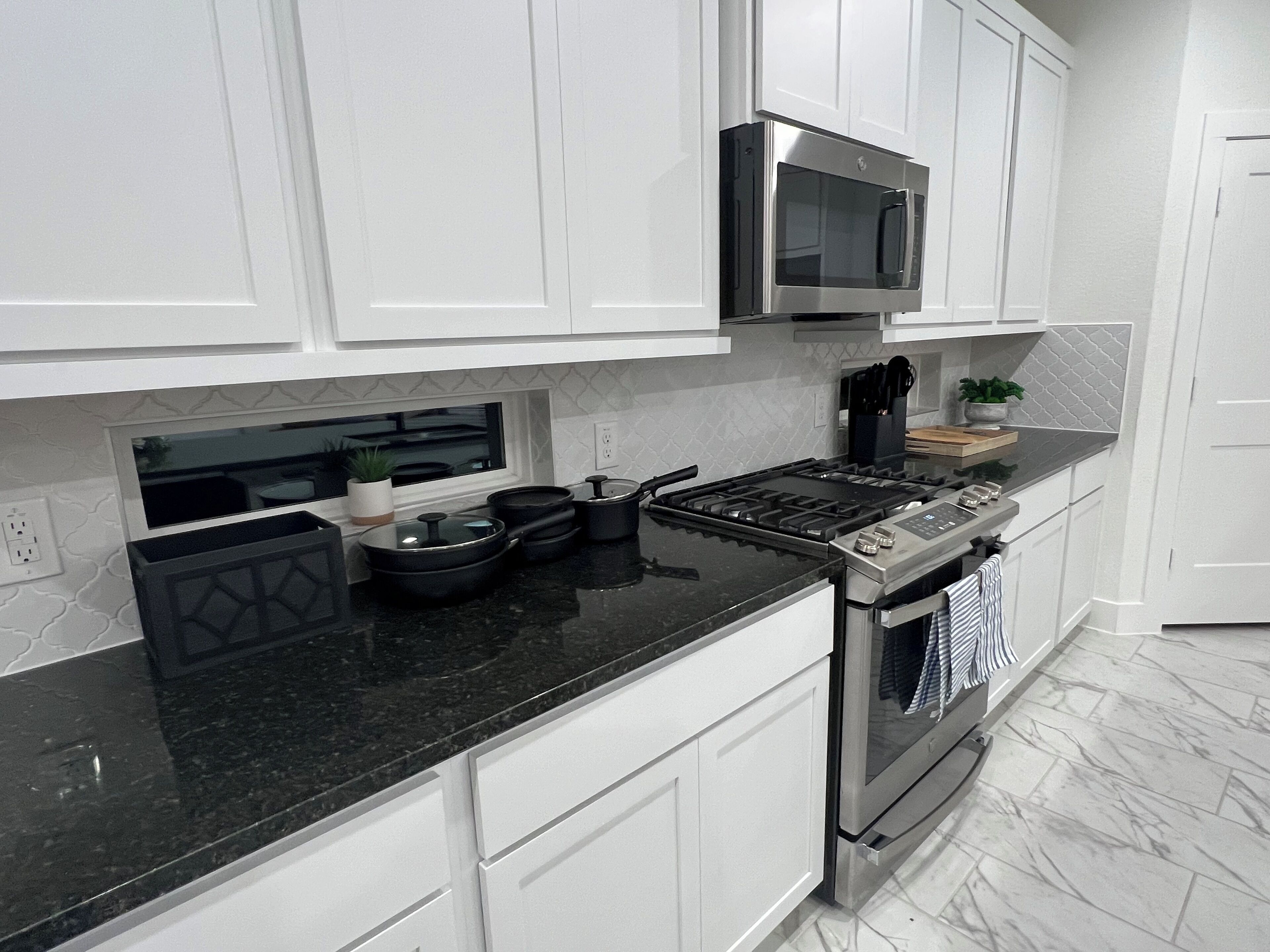 Una cocina moderna con armarios blancos, encimera negra, electrodomésticos de acero inoxidable y una ventana sobre el fregadero.