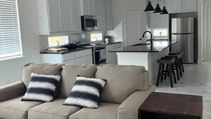 A modern kitchen with white cabinets, a central island, and a dining area with a sofa and stools. - Relax in Style at Our Missouri City Getaway (Missouri City)