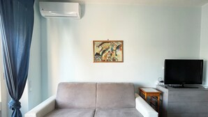 A living room with a beige sofa, a flat-screen TV, a small wooden side table, and a painting on the wall. - Bibbi's House San Lorenzo (Rome)