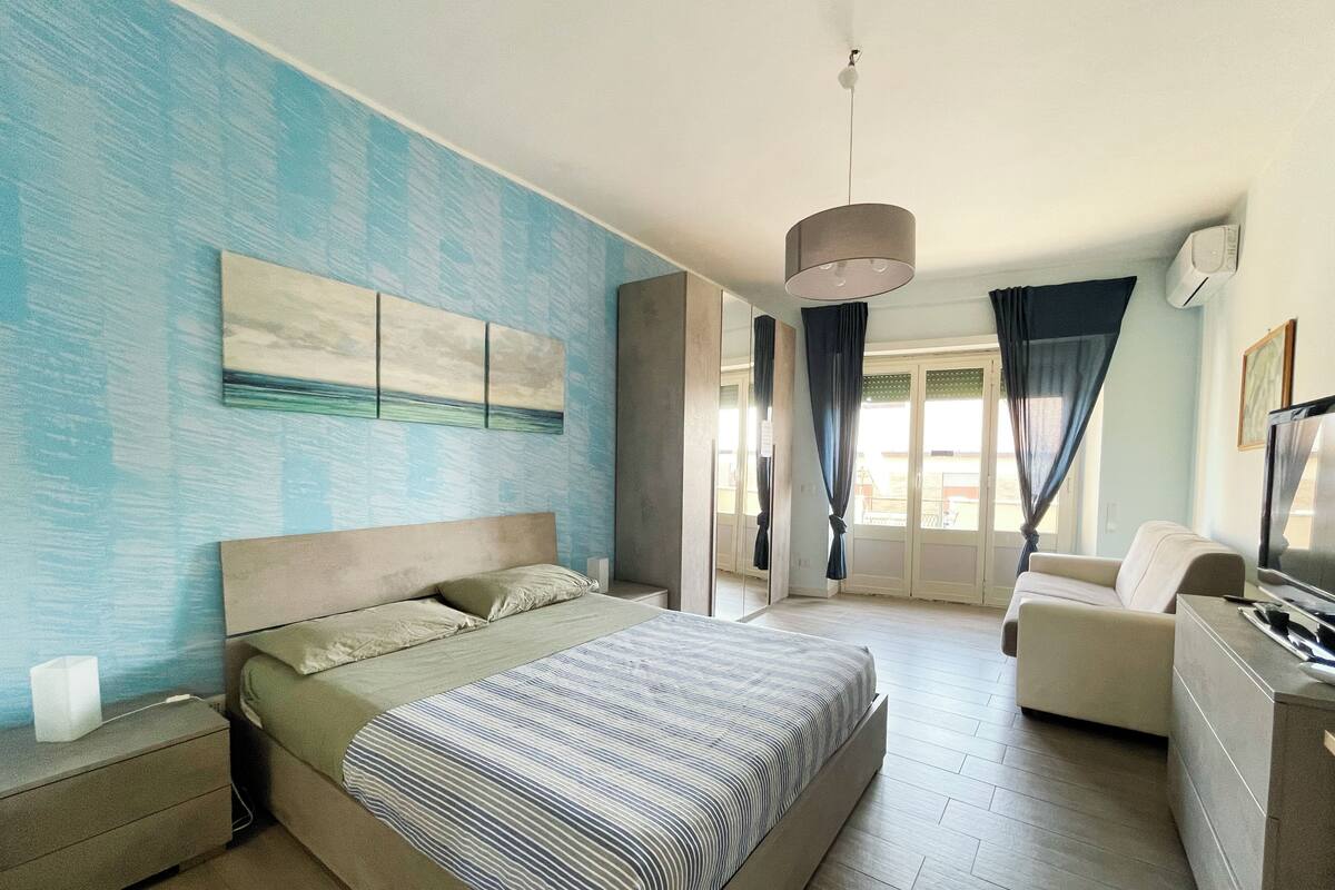 Een moderne slaapkamer met een groot bed, een bank, een televisie en een balkon met gordijnen.